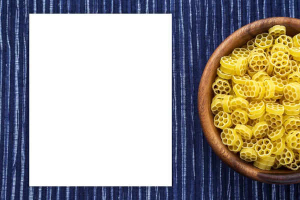 Makkaroni Ruote Pasta in einer hölzernen Schüssel auf einem gestreiften weiß-blauen Stoffhintergrund mit einer Seite. Nahaufnahme mit der Spitze. weißer Raum für Text und Ideen. — Stockfoto