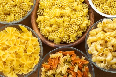 Kahverengi bir rustik arka planda, üstten yakın çekim görünüm makarna ruote bir cam ve ahşap kase farklı makarna makarna ile spiral.