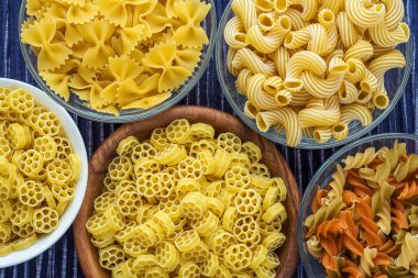 Makarna ruote beyaz tahta ve cam kase ile çeşitli makarna spiraller mavi dokulu bir arka plan üzerinde üst yakından görmek.