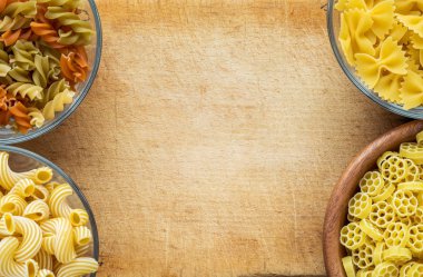 Makarna ruote bir cam ve ahşap kase farklı makarna makarna ile kahverengi rustik ahşap zemin, üstten yakın çekim görünüm spiral. Metin için boş alan.