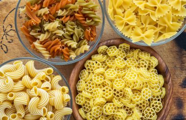 Makarna ruote bir cam ve ahşap kase farklı makarna makarna ile dekore edilmiş rustik ahşap zemin, üstten yakın çekim görünüm spiral.