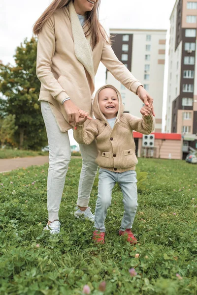 Жінка-мама грає з маленьким сином 4-5 років, восени в місті, на фоні будівлі, повсякденного одягу. Весело грати сміючись, радіючи, позитивні емоції. Бежевий светр з капюшоном . — стокове фото