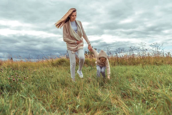 Ibu wanita dengan anak laki-laki berusia 4-5 tahun, di lapangan. Berjalan dan bersantai di akhir pekan di alam, dengan pakaian hangat di musim gugur, dengan sweater berkerudung. Ruang kosong untuk teks . — Stok Foto