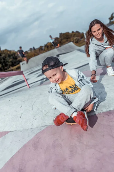 Malý chlapec syn 4-5 let, Mladá matka žena, učí jezdit na skateboardu, letní podzim v městském parku hřiště. Skateboard, neformální oblečení. Podpora vyvážení školení. Emoce radosti zábavy. — Stock fotografie