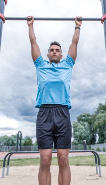 Erkek sporcu, şehirde yaz günü yatay barda kendini yukarı çeker. Aktif gençlik yaşam tarzı, sokaklarda spor. Güç ve motivasyon kavramı. Güçlü erkek lider.