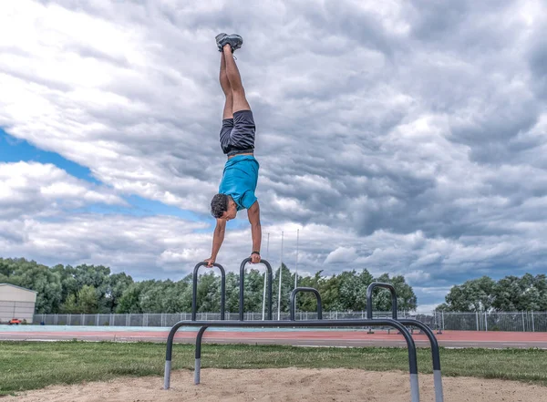 Hombre atleta, soporte de manos, fondo deportes tierra nubes árboles, día en verano en la ciudad. Estilo de vida juvenil activo, ejercicio físico en la calle. Espacio libre para la fuerza y motivación. Entrenador hombre fuerte . —  Fotos de Stock