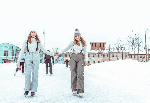 Selamat tersenyum, istirahatlah akhir pekan. Dua gadis pacar musim dingin naik skating pakaian olahraga hangat, topi sweater jumpsuit. Gelanggang es kota, salju latar belakang salju. Emosi sukacita kebahagiaan menyenangkan . — Stok Foto