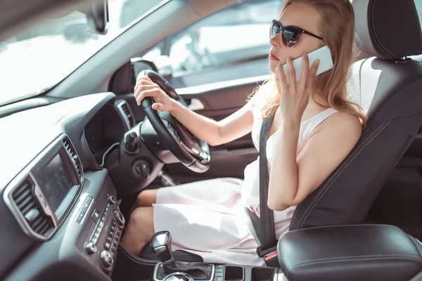 Egy lány vezeti az autót a faházban. Jobb kormányos, bal kormányos. Telefonál, áll a forgalomban, várakozik az utasra, megadja a találkozási helyet. Meghallgatja az üzenetet alkalmazás online hívás. — Stock Fotó