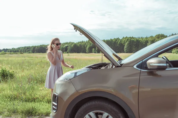 Menina vestido rosa, carro com capuz aberto em linhas laterais estrada de verão perto do campo, fundo grama floresta carro quebrou, acidente parada de emergência, chamando telefonemas reboque caminhão e serviço de reparação especial . — Fotografia de Stock