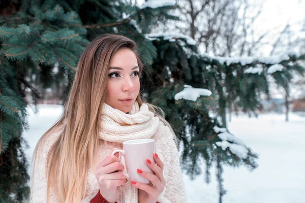 Vacker flicka med mugg händerna, vinter gata i parken, te värms upp med varm dryck kaffe, hon ser glad, drömmar fantasier. Camping nyår semester. Bakgrund snö driver julgran. — Stockfoto