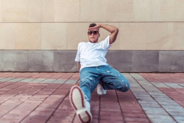 Erkek atlet, uzakta oturuyor, yaz şehri, hip-hop tarzı, break dansçı. Boş alan motivasyon metni. Aktif gençlik yaşam tarzı, modern moda hipster, sokak dansçısı. Tişört kot pantolon güneş gözlüğü.