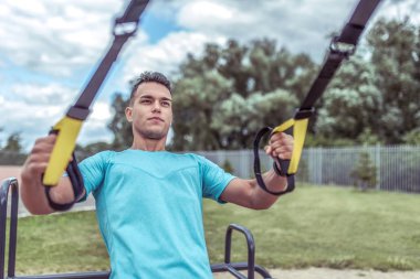 Bir erkek sporcu şehirde yaz günü şınav ve barfiks çekmek için kemer takıyor. Aktif gençlik yaşam tarzı, sokaklarda spor. Güç motivasyonu için yakın plan. Güçlü antrenör..