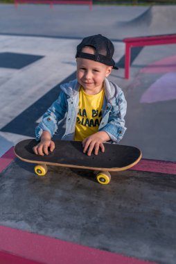 3-5 yaşlarında mutlu bir çocuk, yazın spor sahasında, neşesine gülümseyen, kaykay öğrenmek için zor öğreniyor. Sonbahar giysileri. Zevk ve rahatlama duyguları..