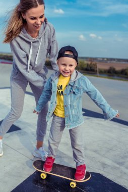 Küçük oğlu olan genç bir anne, mutlu bir aile kaykay sürmeyi öğreniyor, yazın açık havada, sonbahar gününde. Zevkin duyguları, mutluluğun ve eğlencenin sevinci. Eğitimde bakım desteği, ebeveynlik.