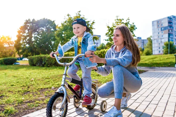 Ibu muda mengajarkan wanita mengendarai sepeda, bermain dengan anak laki-laki berusia 3-5 tahun, tertawa gembira menikmati tersenyum, musim panas di taman kota, pakaian musim gugur alam, emosi kelembutan cinta dan perhatian . — Stok Foto