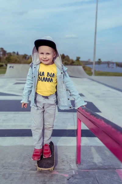 Anak kecil naik skateboard di musim panas di kota. Selamat tersenyum. Celana Kasual denim. Pelajaran keseimbangan pada papan tulis . — Stok Foto