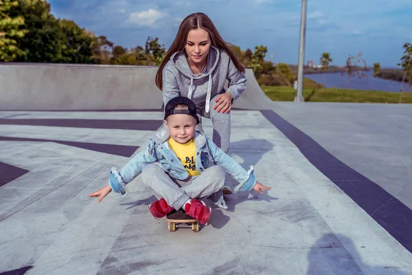 Ibu muda dengan anak laki-laki kecil, keluarga taman bermain belajar naik skateboard, musim panas di luar ruangan, hari musim gugur. Emosi yang menyenangkan, kebahagiaan yang menyenangkan. Membantu dalam pelatihan, mengasuh anak . — Stok Foto
