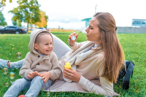 Lycklig familj, ung mor kvinna, liten pojke son 3-6 år gammal, känslor glädje positiv. Beige vardagskläder. Blås luftbubblor, spela koppla av på helgen varma casual wear, beige tröja med huva — Stockfoto