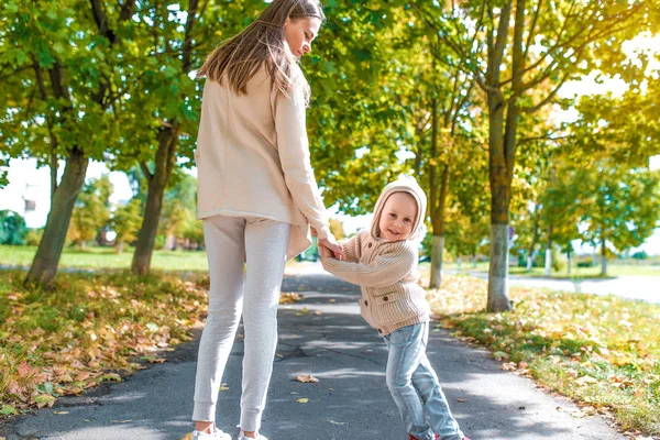 Žena matka chodí, drží ruku malého chlapce syna, podzim ve městě, procházka v parku, tráva pozadí, teplé ležérní oblečení, béžový svetr s kapucí. Emoce štěstí jsou zábavné a relaxační. — Stock fotografie