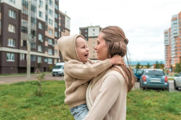 Ibu wanita menggendong anak dalam pelukannya, berjalan, beristirahat di kota pada musim gugur, pakaian hangat kasual, sehari di jalan. Happy tertawa dan tersenyum . — Stok Foto