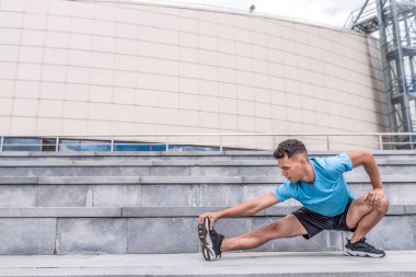 Yaz sabahı antrenmanından önce kaslarını esneten erkek sporcu, arka plan basamakları inşa ediyor. Aktif gençlik yaşam tarzı, spor yapma doğası. Boş alan metin gücü ve motivasyonu.