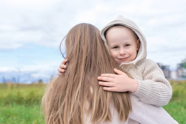 Liten pojke på hösten på gatan, kramar kvinna mamma, känslor hjälper stödja omsorg och kärlek till sitt barn. Varma kläder på kall dag, beige kofta med huva. — Stockfoto