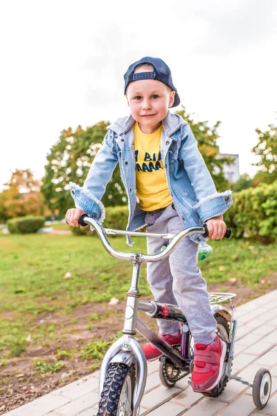 Glad liten pojke 3-5 år gammal, på sommaren i stadsparken, ler jublar, lär sig cykla, lär sig hur höstkläder. Känslor av nöje och avkoppling. — Stockfoto