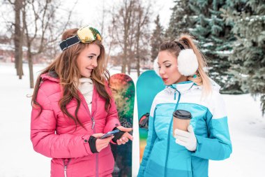 İki kız arkadaş, Winter Park tatil köyü, cep telefonu. Rahatlamak, sıcak içecekler ve kahve ile ısınma hakkında konuşmak. Duygular zevk rahatlık. Spor tulumları, arka plan kar ağaçları ve snowboardlar..