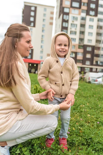 Genç mutlu aile, kadın anne ve küçük oğul. El ele tutuşun, sonbahar geldi, gülümsüyor, yürüyor ve seviniyor. Kapüşonlu kazaklı, rahat kıyafetler.. — Stok fotoğraf