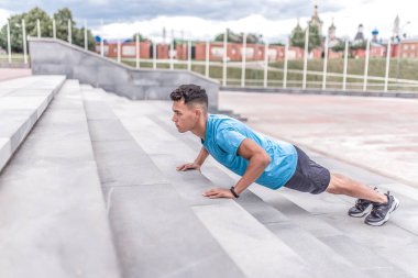 Sporcu adam beton basamaklardan tırmanıyor, yazın şehirde antrenman yapıyor, aktif bir yaşam tarzı, modern fitness egzersizi. Motivasyon metni için boş alan.