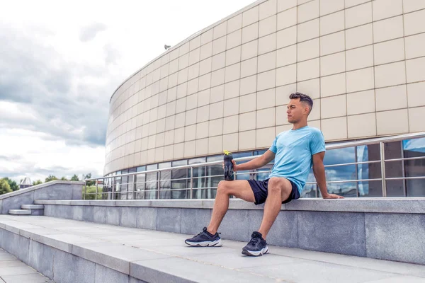 sports man resting after hard workout, shaker with protein and water, a daytime workout in city, active lifestyle, modern fitness workout. Free space.