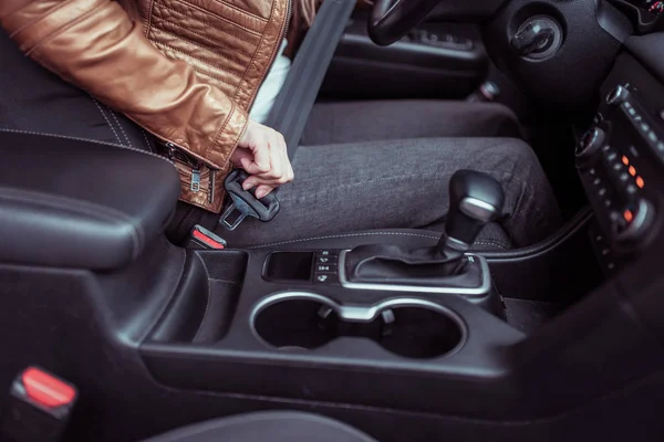 Close-up, carro de condução mulher prende seu cinto de segurança, jaqueta de couro marrom, transmissão automática, no outono inverno na cidade no estacionamento, segurança no trânsito, ativação de airbags em um acidente . — Fotografia de Stock