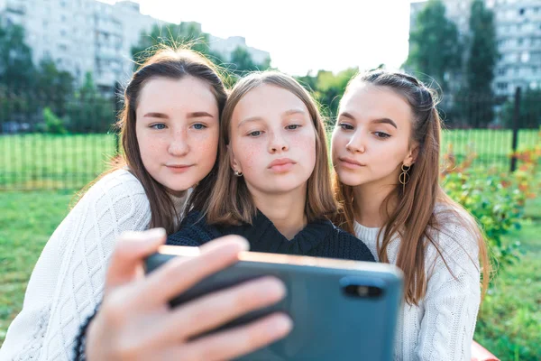 Trzy uczennice w wieku 13-15 lat, jesienny letni dzień w mieście, fotografowanie się przez telefon, szczęśliwy uśmiech, luźne ubrania, odpoczynek po przerwie w szkole. Online sieci społecznościowych selfie. — Zdjęcie stockowe