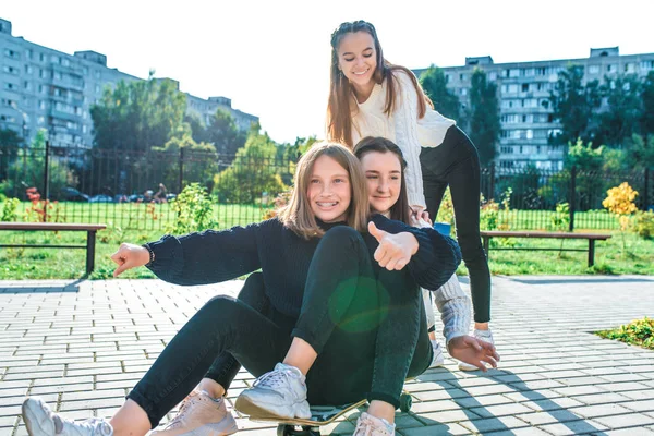 Tiga gadis sekolah 13-15 tahun, musim panas musim gugur di kota, naik skateboard, senang tertawa, pakaian santai, beristirahat setelah libur sekolah. Emosi menyenangkan kesenangan remaja . — Stok Foto