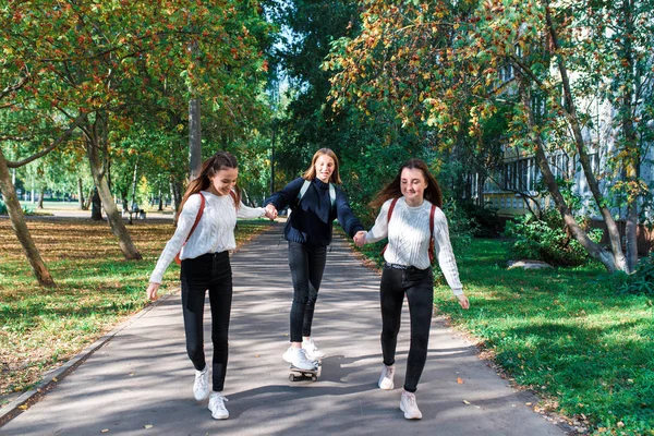 Drie meisjes schoolmeisjes tieners 13-15 jaar oud, herfst zomerdag stad, rijden skateboard, gelukkig glimlachen, casual kleding, rust na schoolvakanties. Emoties plezier en plezier. — Stockfoto