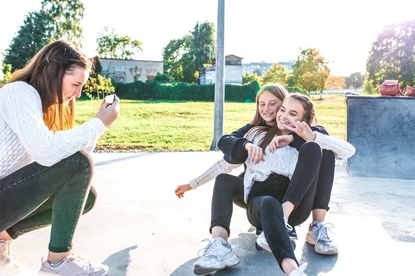 Tři dívky školačky teenageři 13-15 let, jezdit na skateboardu, fotit selfie na telefonu. Emoce radosti radost radost radost, šťastní se usmívají, ležérní oblečení, relaxace po škole na dovolené. — Stock fotografie