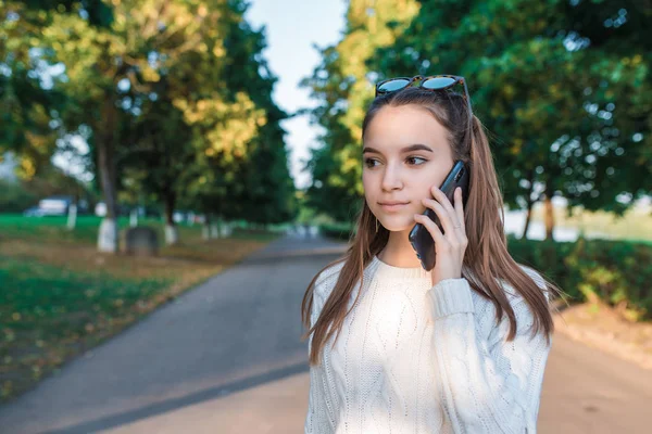 Gadis remaja berusia 13-15 tahun, kota musim gugur musim panas, orang tua menelepon telepon, sweater pakaian santai, pesan suara mendengarkan, aplikasi jejaring sosial Internet. Emosi menghibur. Teks ruang kosong . — Stok Foto