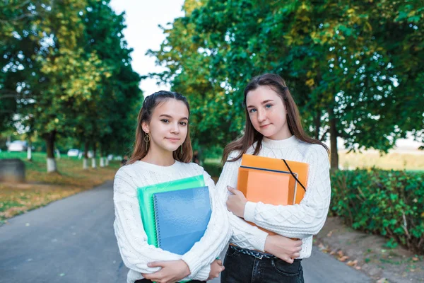 Две девочки школьницы 12-15 лет, осенний летний город, руки тетради папки с заметками, счастливые улыбающиеся умные студенты, повседневная одежда, свитер, портрет школьницы-подростка на природе . — стоковое фото