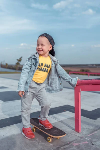 Anak kecil di musim panas di kereta api kota dan belajar untuk naik skateboard, di musim gugur di lapangan olahraga, tersenyum bahagia dalam pakaian kasual . — Stok Foto