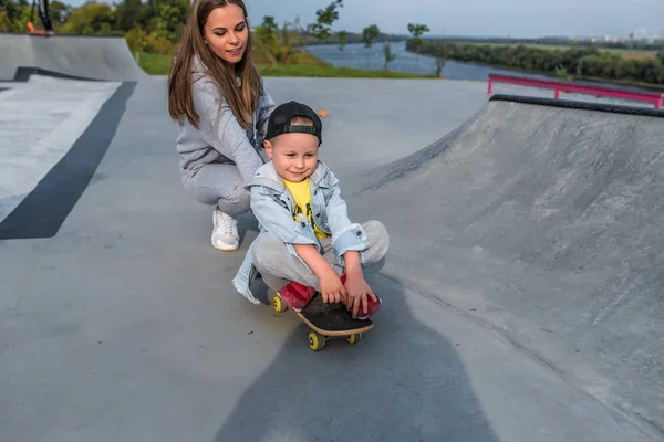 Ibu keluarga anak laki-laki berusia 3-5 tahun, olahraga musim panas di kota, bermain skateboard, emosi sukacita, relaksasi menyenangkan pada akhir pekan. Pakaian sehari-hari, mengasuh anak. . — Stok Foto