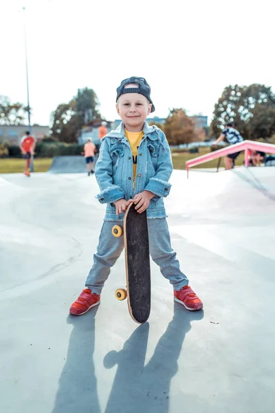 3-5岁的小男孩，夏天在城市的运动场上，秋天在户外，快乐的微笑，快乐的玩耍，练习滑板，休闲装，棒球帽牛仔裤。 周末休息. — 图库照片