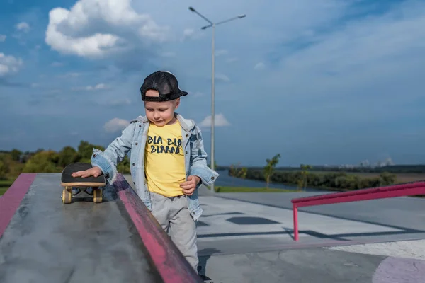 Anak kecil berusia 3-5 tahun, musim panas di lapangan olahraga di kota, musim gugur di jalan, bermain skateboard, berlatih skateboard, pakaian kasual, topi bisbol dan celana jeans. Istirahat akhir pekan . — Stok Foto