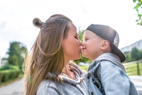Женщина мама целует маленького мальчика сына 3-5 лет, играть весело обнимает, летом в городе, осенью в парке, случайная одежда. Забота и воспитание любви к ребенку . — стоковое фото
