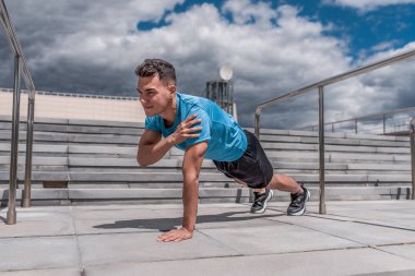 Erkek sporcu karın kası baskısı antrenmanı, spor eğitimi, şehirde yaz tatili. Gençlik yaşam tarzı spor motivasyonu. Spor kıyafetleri, şortlar ve spor ayakkabılı bir tişört. Bulut merdiven arkaplanı.