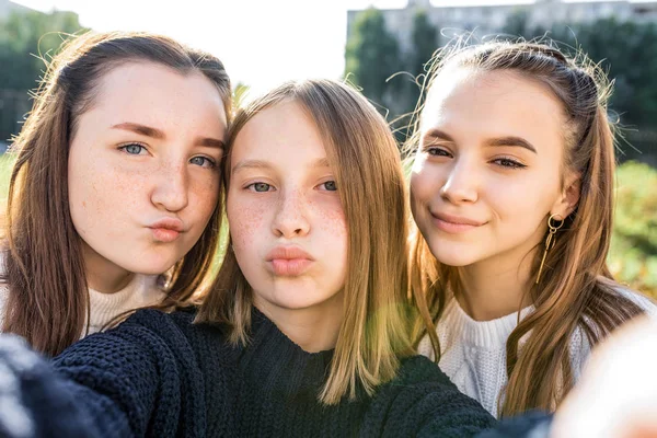 3 dívky přítelkyně teenageři, 14-15 let, fotografování selfie na telefonní kameru, v podzimní den ve městě na ulici, odpočívá po škole a vysoké škole. V každodenním oblečení, svetru. — Stock fotografie