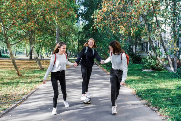 3 gadis remaja, naik skateboard, jalanan kota hari, senyum bahagia, bersenang-senang setelah kuliah. Emosi hiburan relaksasi, berjalan santai memakai. Sweater celana jeans. . — Stok Foto
