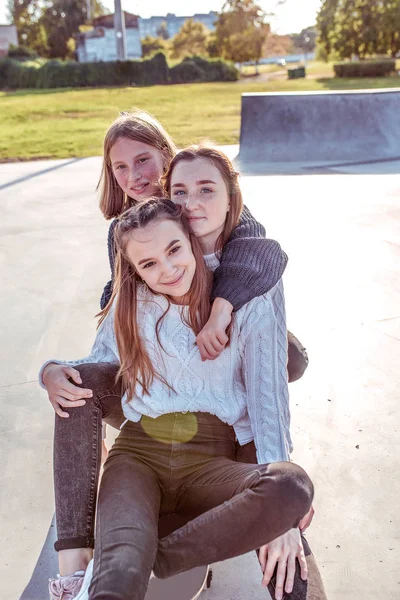 3 pacar perempuan, senang duduk dan tersenyum, remaja sepulang sekolah, santai naik skateboard, kota sore, bersukacita bersenang-senang. Emosi hiburan relaksasi, kasual memakai celana jeans sepatu olahraga di sweter . — Stok Foto