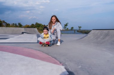 Genç kadın anne kaykay öğretmeni, küçük oğlan, kaykay. Metni kopyalamak için boş alan. Hafta sonu parkta dinlenin. Her gün kalın giysiler, sonbahar günü. Mutlu gülüşler gülüşler ve neşe.