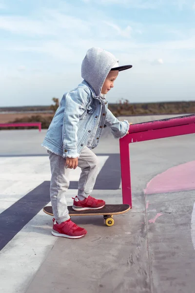 Liten pojke 3-5 år gammal, lära sig att rida skateboard, höstdag, casual varma kläder. Denim tröja med huva. Körlektioner, första upplevelsen, utomhussport. — Stockfoto