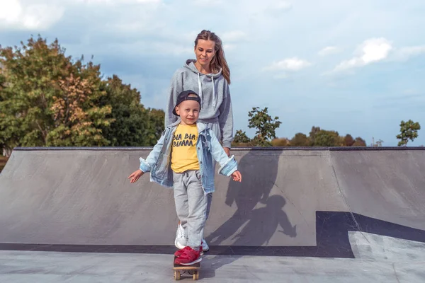 Ibu muda mengajar skateboard, anak kecil, skateboard. Istirahat pada akhir pekan di jalan di taman. Setiap hari hangat pakaian, musim gugur hari. Senyum bahagia tertawa dan bersukacita. Ruang kosong untuk menyalin teks . — Stok Foto